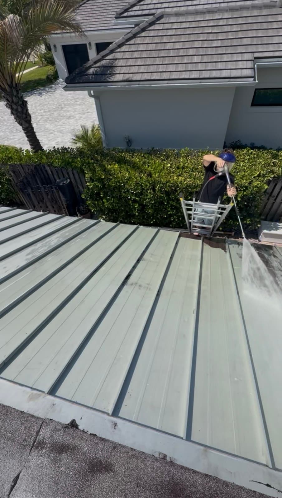 After — a Fresh Frames technician soft-washing the metal roof back to clean, bright metal with low-pressure, growth-killing wash