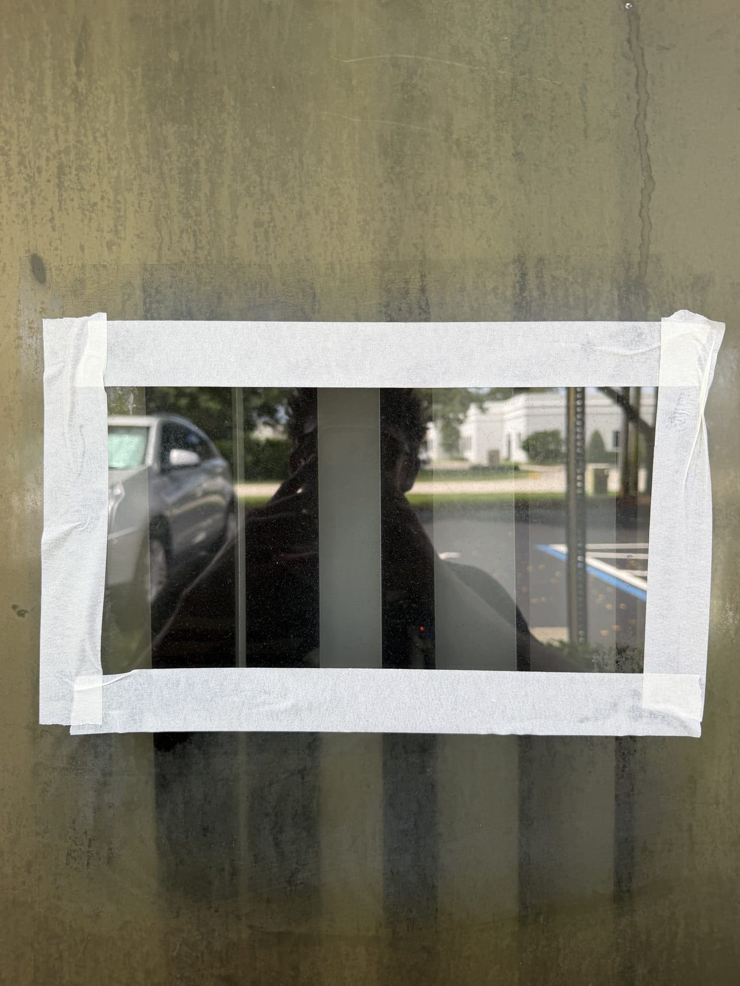 After — the same taped test patch restored to crystal-clear glass, the parking lot and building behind it sharp while the untreated glass around it stays hazy