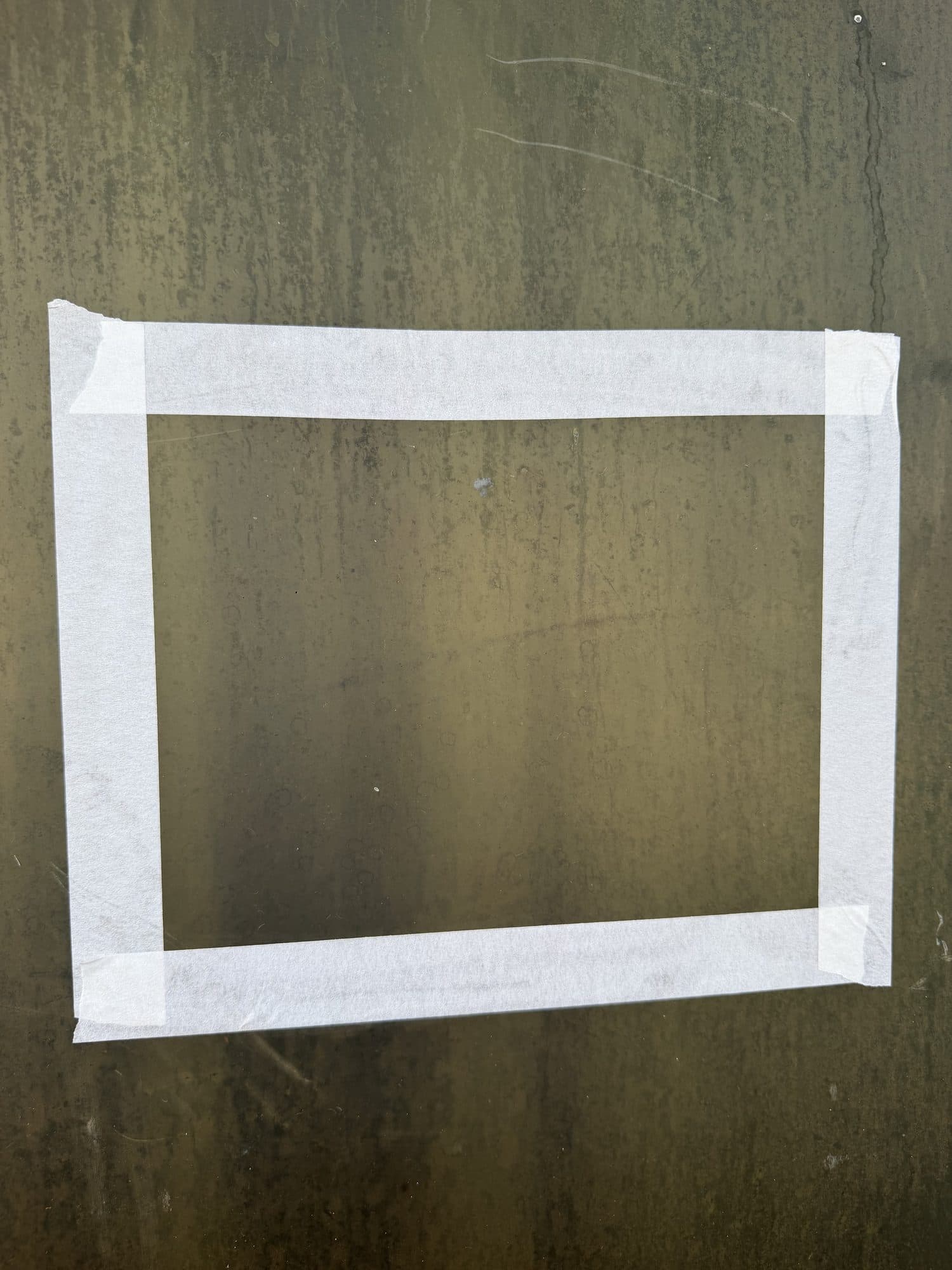 Before — a Florida storefront pane clouded olive-brown with baked-on hard-water film, oxidation and mineral streaks, a taped test patch marking the area to be restored